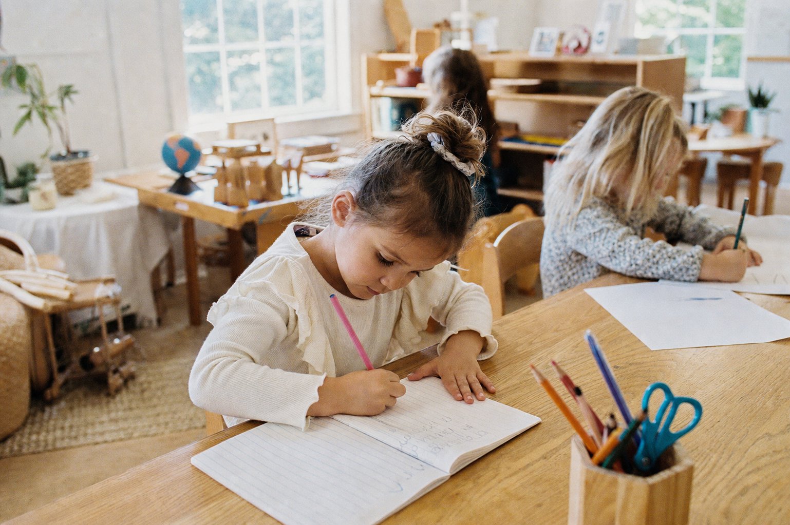 A Pre-K child writing at a wood table